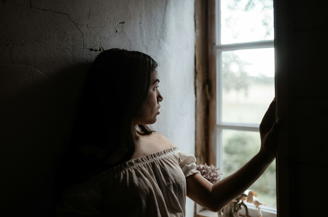 Woman with dark hair reading a book by a window